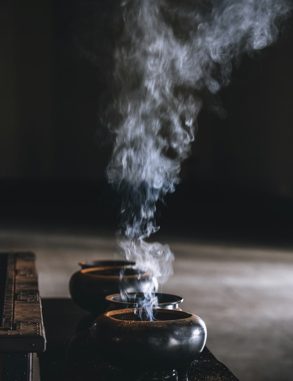 Smoke rising from dark vessels — the oud and resins that make up the drydown.
