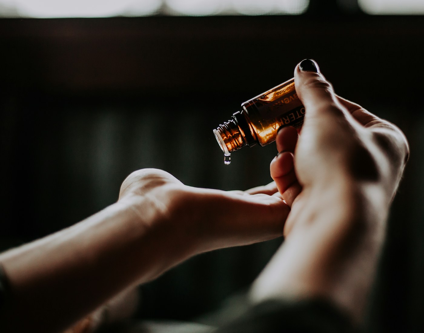 A drop of amber essence falling from the flacon into an open palm, in low light.